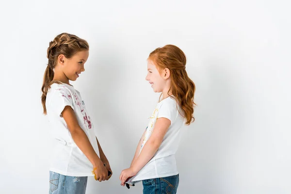 Vista laterale di bambini felici con vernice su t-shirt in piedi su bianco — Foto stock