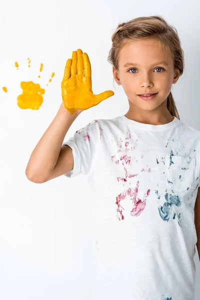 Cute kid showing yellow paint on hand near yellow hand print on white — Stock Photo