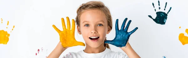 Панорамный снимок возбужденного ребенка с краской на руках рядом с отпечатками рук на белом — стоковое фото