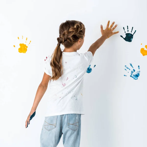 Vista trasera del niño poniendo la mano cerca de las huellas de las manos en blanco - foto de stock