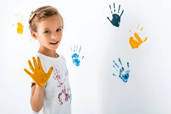 Happy kid with yellow paint on hand near hand prints on white — Stock Photo