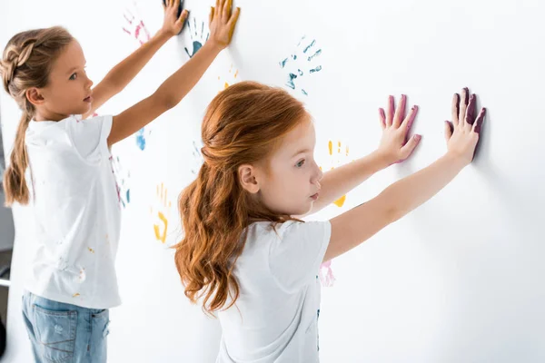 Селективный фокус рыжеволосого ребенка, помещающего отпечатки рук рядом с ребенком на белом — стоковое фото