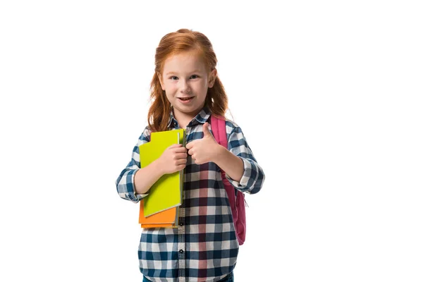 Счастливый рыжий ребенок с книгами и показывая большой палец на белом — стоковое фото