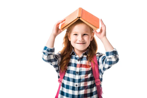 Joyeuse pupille rousse tenant livre orange au-dessus de la tête isolé sur blanc — Photo de stock