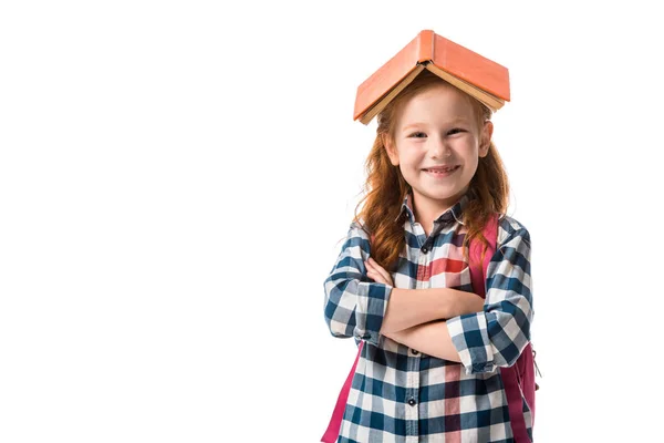 Cheerful redhead pupil with orange book on head standing with crossed arms isolated on white — Stock Photo