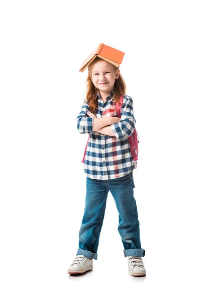 Cheerful redhead kid with orange book on head standing with crossed arms isolated on white — Stock Photo