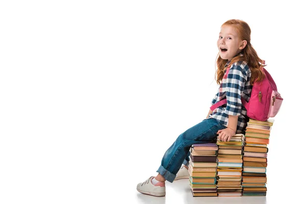 Surprised redhead schoolkid sitting on books on white — Stock Photo