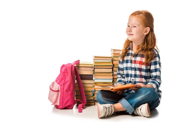 Positive rothaarige Schulkind sitzt neben Büchern und rosa Rucksack auf weiß — Stockfoto