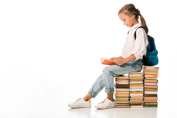 Fröhliches Schulkind, das auf Büchern sitzt und weiß liest — Stockfoto