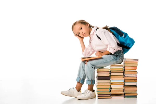 Nettes Schulkind sitzt auf Büchern und schaut in die Kamera auf weiß — Stockfoto