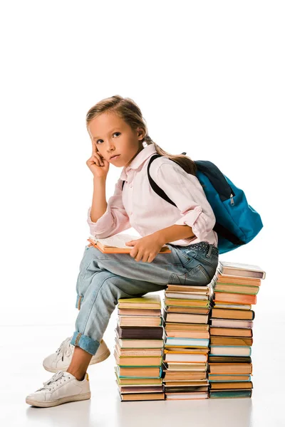 Entzückendes Schulkind sitzt auf Büchern und schaut in die Kamera auf weiß — Stockfoto