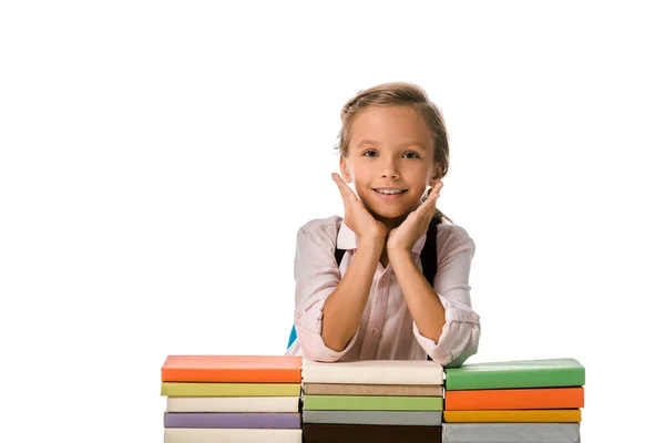 Позитивний школяр дивиться на камеру біля барвистих книг ізольовані на білому — стокове фото