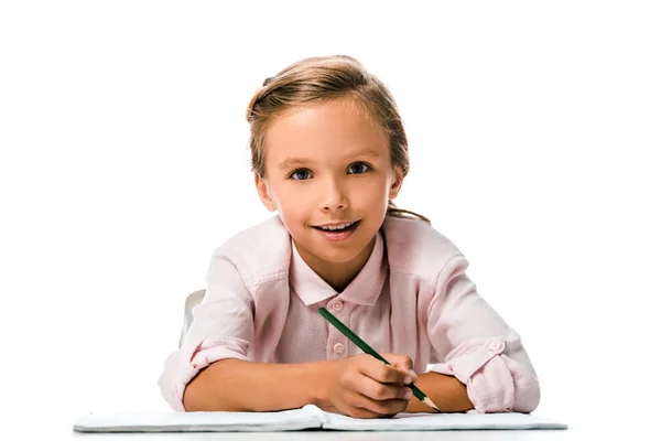 Alegre colegial sonriendo y sosteniendo lápiz cerca de cuaderno aislado en blanco - foto de stock
