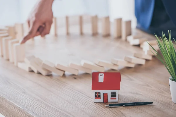 Partial view of risk manager blocking domino effect of falling wooden blocks near house model — Stock Photo
