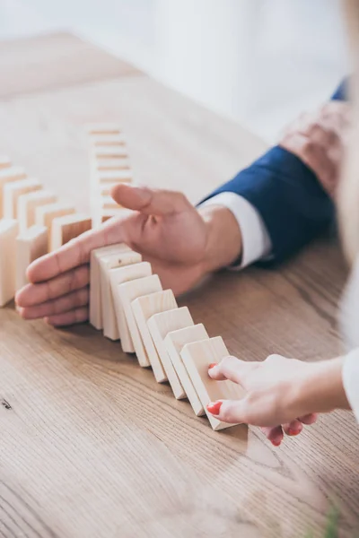 Cropped view of woman pushing wooden block and risk manager blocking domino effect — Stock Photo