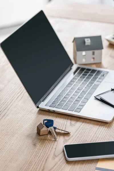 Laptop and smartphone with blank screen, keys and house model on wooden table — Stock Photo