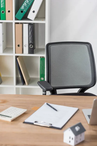 Foyer sélectif de chaise de bureau et rack avec des dossiers près du bureau avec presse-papiers, calculatrice et maison — Photo de stock