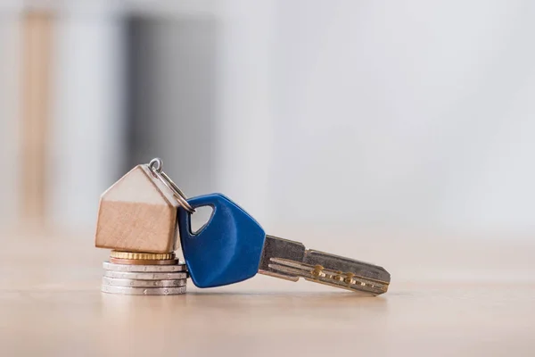 Llave con la baratija de la casa del juguete en la pila de monedas de holden y de plata en la mesa de madera - foto de stock