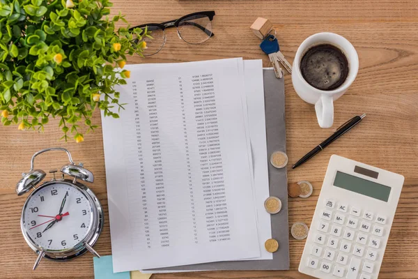 Top view of wooden table with document, coffee cup, alarm clock, house keys, calculator and green plant — Stock Photo