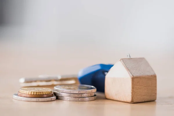 Selective focus of toy house trinket with keys near golden and silver coins on wooden table — Stock Photo