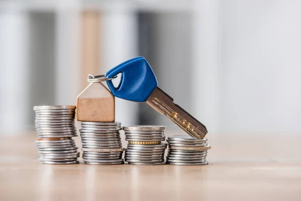 Key with toy house trinket on stacks of golden and silver coins on wooden table — Stock Photo