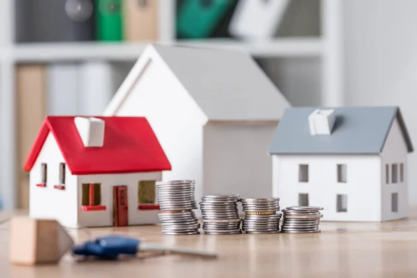 Selective focus of stacked coins near house models and keys on wooden table — Stock Photo