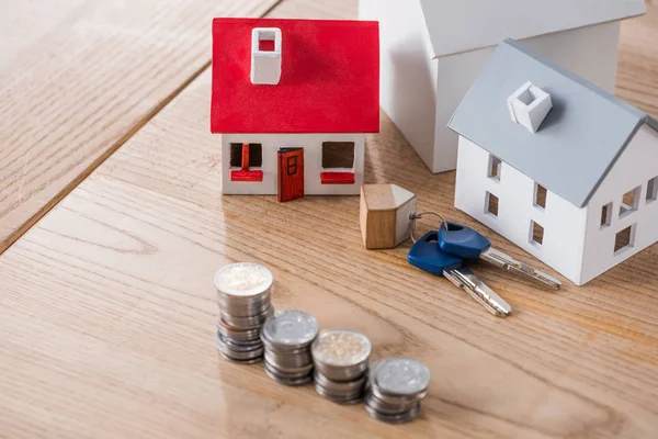 House models near keys and stacks of golden and silver coins on wooden table — Stock Photo