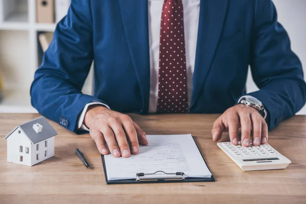 Vue recadrée de l'homme d'affaires dans l'usure formelle en utilisant la calculatrice et l'écriture dans le contrat près de maison modèle — Photo de stock