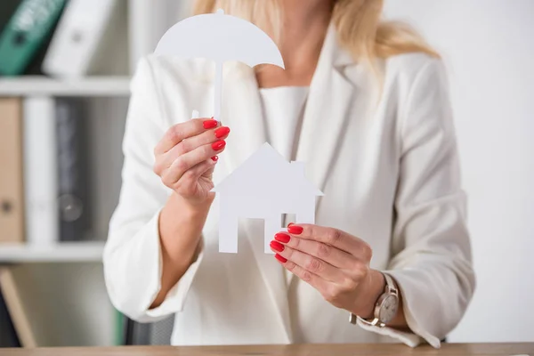 Partial view of businesswoman showing white paper cut house and umbrella — Stock Photo