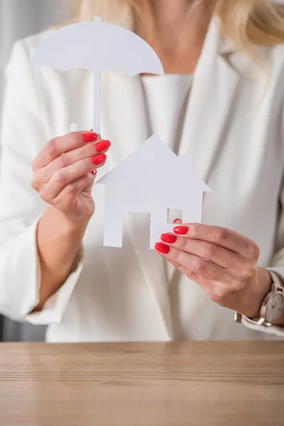 Vue recadrée de femme d'affaires montrant la maison et le parapluie coupés en papier blanc — Photo de stock