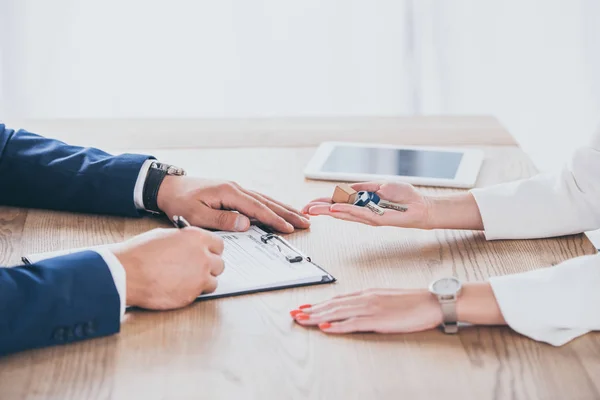 Vue recadrée de femme d'affaires tenant clés de maison près de l'homme accord de signature — Photo de stock