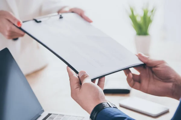 Partial view of businesswoman giving clipboard to colleague sitting at workplace — Stock Photo