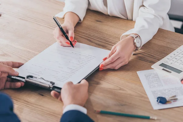 Cropped view of businessman holding clipboard and woman signing contract — Stock Photo