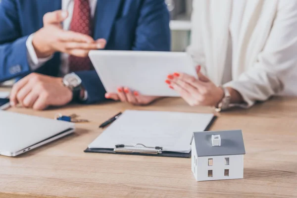 Enfoque selectivo de modelo de casa cerca de mujer sosteniendo tableta digital y hombre de negocios apuntando con la mano - foto de stock