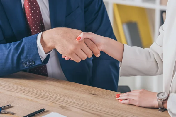 Partial view of businessman shaking hands with woman while sitting at wooden desk — Stock Photo