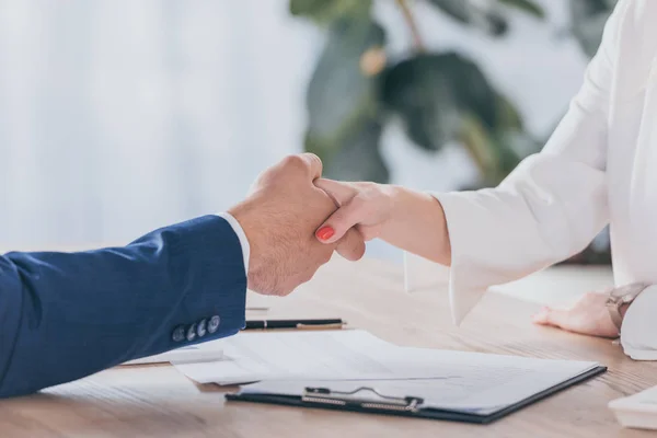 Teilansicht einer Geschäftsfrau, die einem Mann die Hand schüttelt, während sie am Holztisch sitzt — Stockfoto