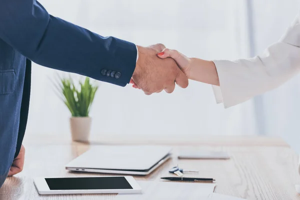 Partial view of businessman shaking hands with woman while sitting at wooden desk — Stock Photo