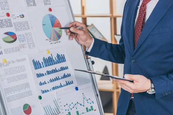 Cropped view of businessman in formal wear analyzing infographics on flipchart — Stock Photo