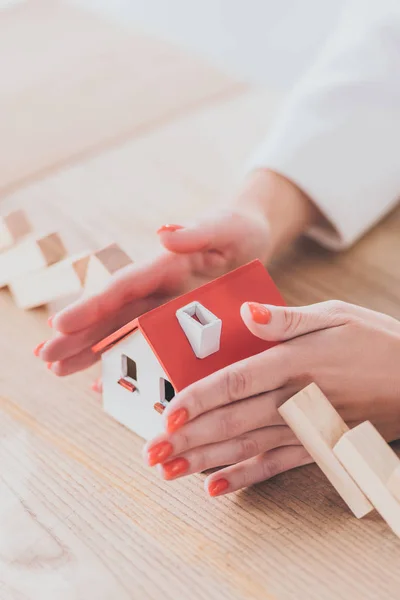 Partial view of businesswoman protecting house model from falling wooden blocks with hands — Stock Photo