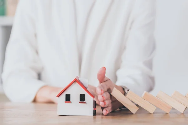 Partial view of risk manager protecting house model from falling wooden blocks with hand — Stock Photo