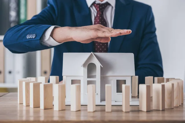 Vista ritagliata del risk manager che copre il modello di casa circondato da blocchi di legno con mano — Foto stock
