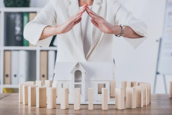 Visão parcial do gerente de risco cobrindo modelo de casa cercada de blocos de madeira com as mãos — Fotografia de Stock