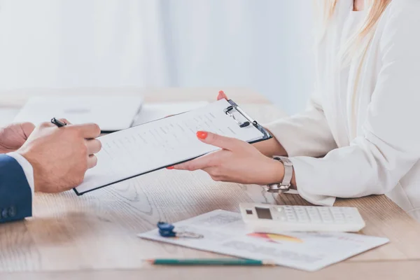 Vista recortada de la mujer de negocios que sostiene portapapeles y el hombre de acuerdo de firma - foto de stock