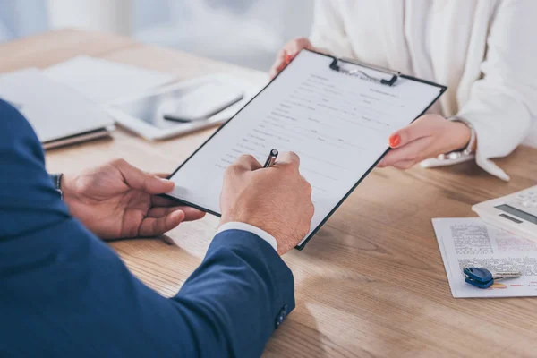 Vue recadrée de femme d'affaires tenant presse-papiers et client accord de signature — Photo de stock