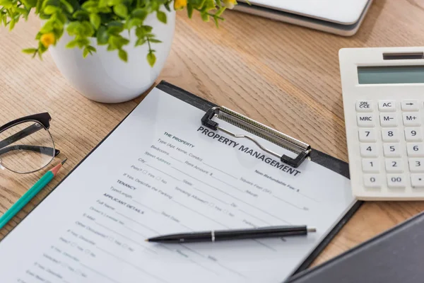 Clipboard with property management agreement, pen, calculator and green plant on wooden desk — Stock Photo