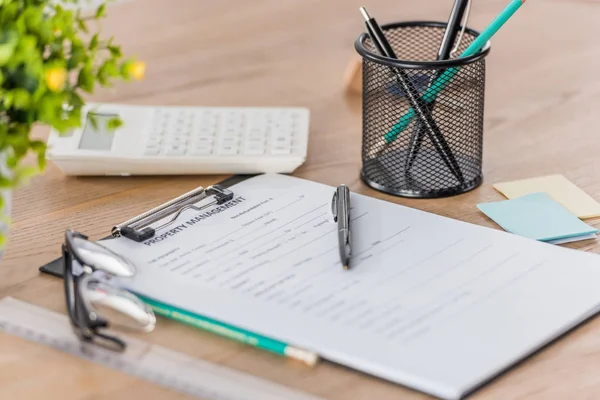 Clipboard with property management agreement, glasses, calculator and pen holder on wooden desk — Stock Photo