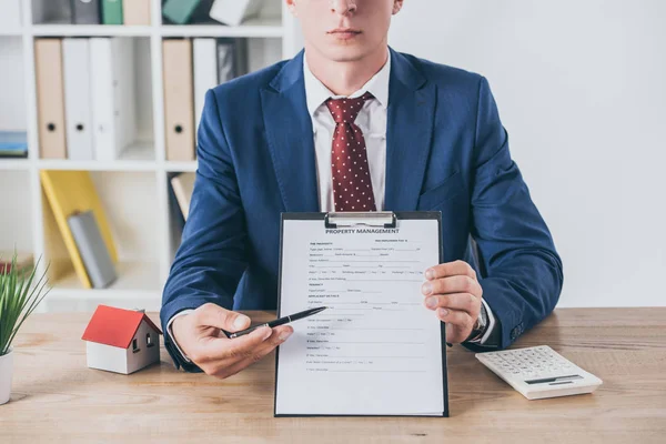 Cropped view of businessman holding clipboard with property management agreement near house model and calculator — Stock Photo