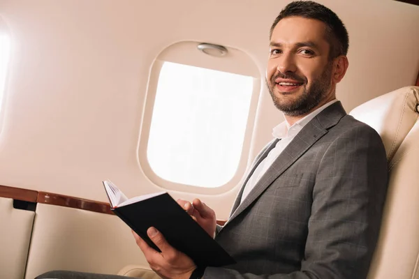 Cheerful businessman holding notebook in private jet — Stock Photo