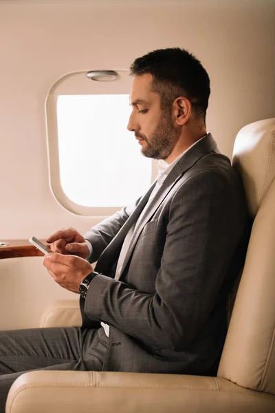 Side view of bearded businessman using smartphone in private jet — Stock Photo