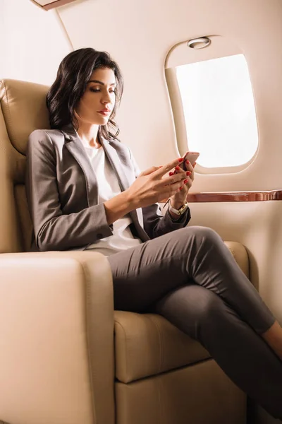 Приваблива бізнесменка користується смартфоном на приватному літаку. — стокове фото
